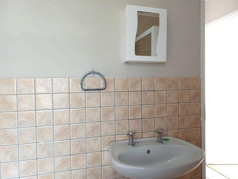 A functional bathroom vanity area featuring a wall-mounted basin, chrome taps, tiled splashback, and a small medicine cabinet.