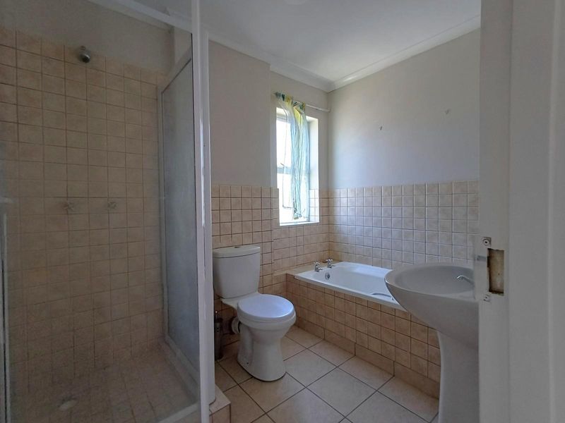 A functional bathroom featuring a separate shower enclosure, a built-in bathtub, a pedestal basin, and a toilet with neutral wall and floor tiling.