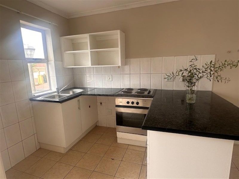 A functional kitchen featuring dark granite countertops, white cabinetry, a built-in oven with hob, and tiled splashbacks.