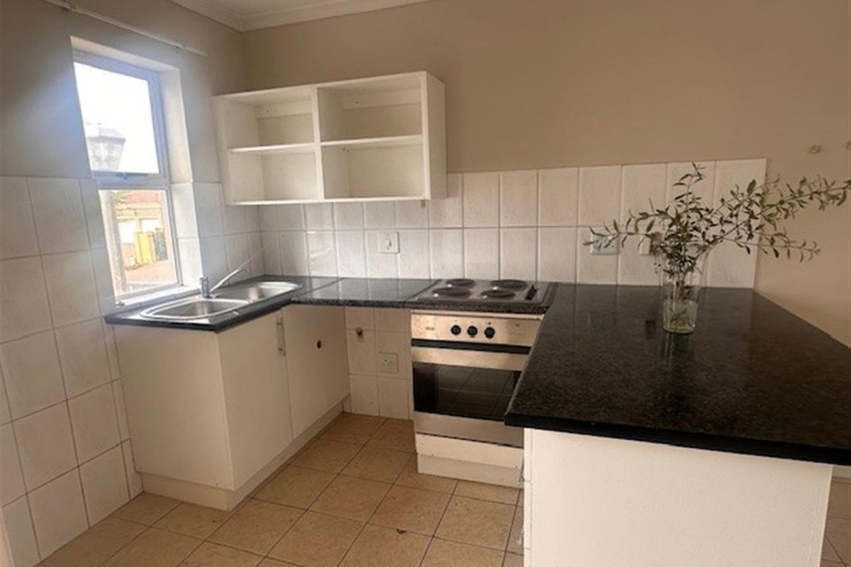 A functional kitchen featuring dark granite countertops, white cabinetry, a built-in oven with hob, and tiled splashbacks.