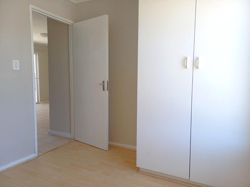 A bedroom featuring light wood-look flooring and a built-in white wardrobe, with an open doorway leading to an adjacent tiled living area.