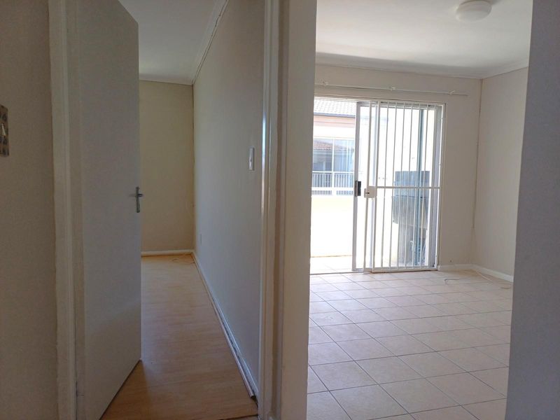 An interior view showing a hallway leading into a living area with tiled flooring and a sliding glass door opening to a patio.