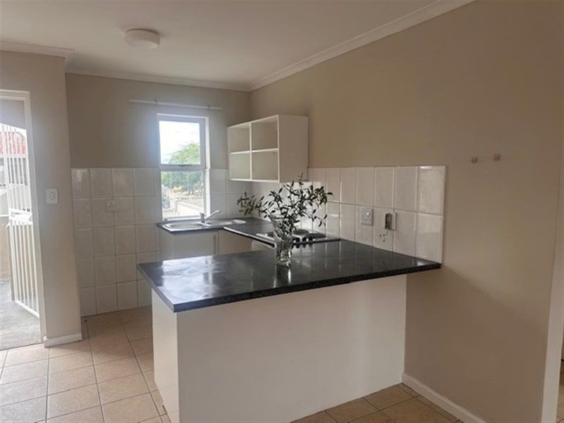 A functional kitchen featuring a breakfast bar, tiled splashbacks, built-in cabinetry, and a stainless steel sink with direct access to an outdoor area.