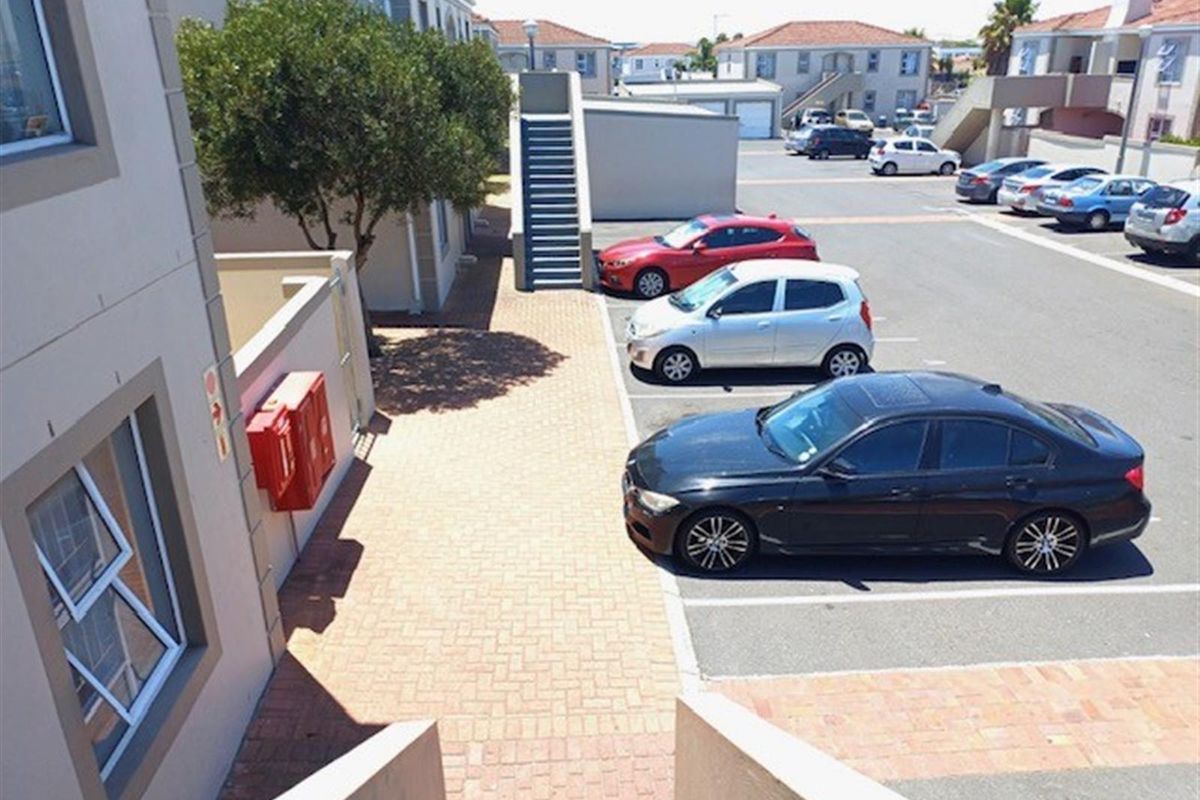 An elevated view of the apartment complex parking area, featuring paved walkways, designated parking bays, and exterior building facades.