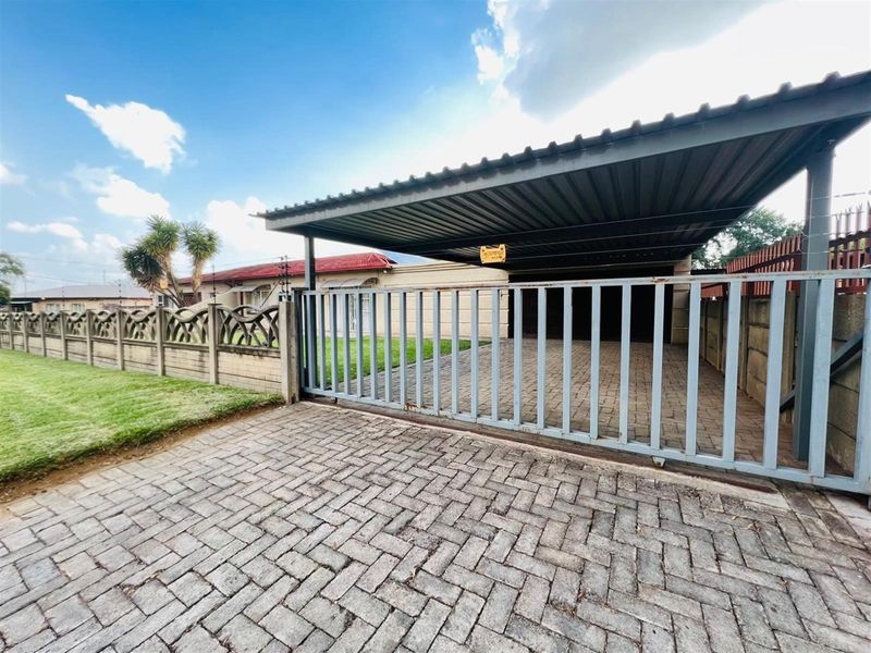 Front exterior view featuring a paved driveway, a covered carport, and a secure sliding gate with precast boundary walling.
