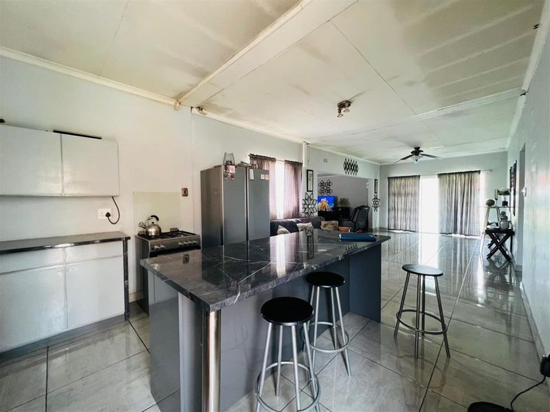 Open plan living and kitchen area featuring a central island with stone countertop, tiled flooring, and sliding glass doors leading to the exterior.
