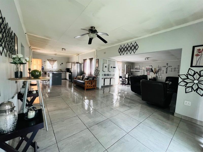 Spacious open-plan living area featuring large format floor tiles, a ceiling fan, and an integrated kitchen layout with ample cabinetry.