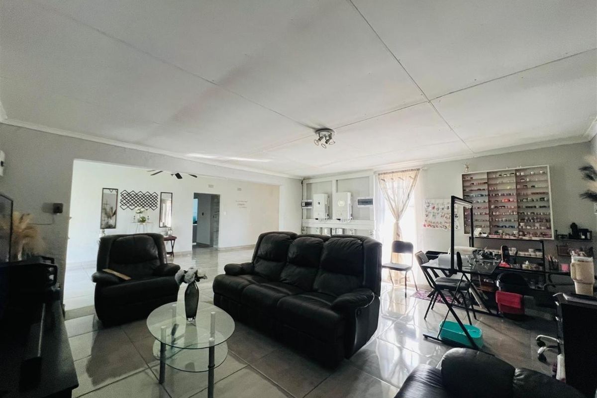 Spacious living area featuring tiled flooring and coved ceilings, currently utilized as a multi-purpose space with wall-mounted electrical infrastructure.