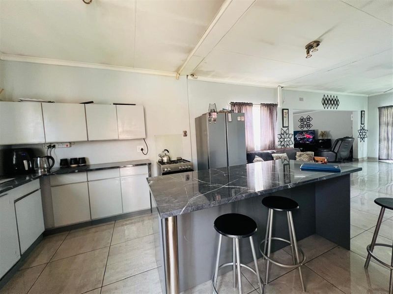 Open-plan kitchen and living area featuring a modern marble-look island, tiled flooring, and functional cabinetry, offering a versatile space for cooking and entertaining.