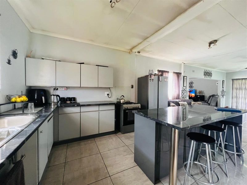 Open plan kitchen featuring modern cabinetry, a central island with stone countertops, and tiled flooring, seamlessly flowing into the adjacent living area.