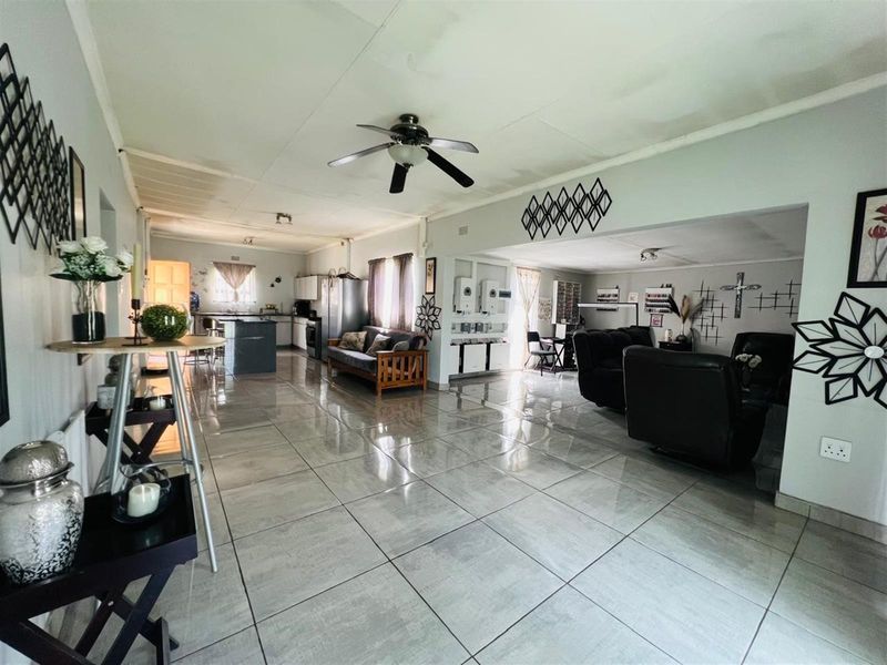 Spacious open-plan living area featuring large format floor tiles, a central kitchen island, and integrated kitchen cabinetry with a ceiling fan.