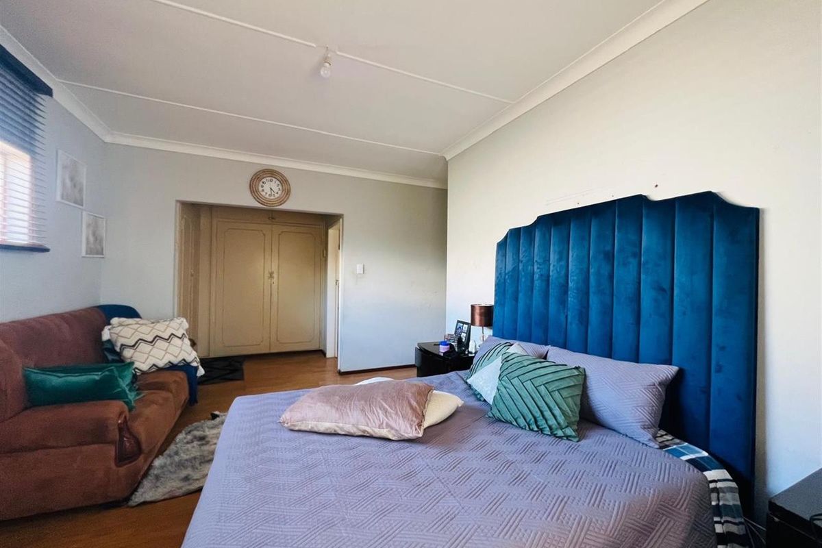 Spacious bedroom featuring laminate flooring, coved ceilings, and built-in cupboards, offering a comfortable layout with space for a seating area.