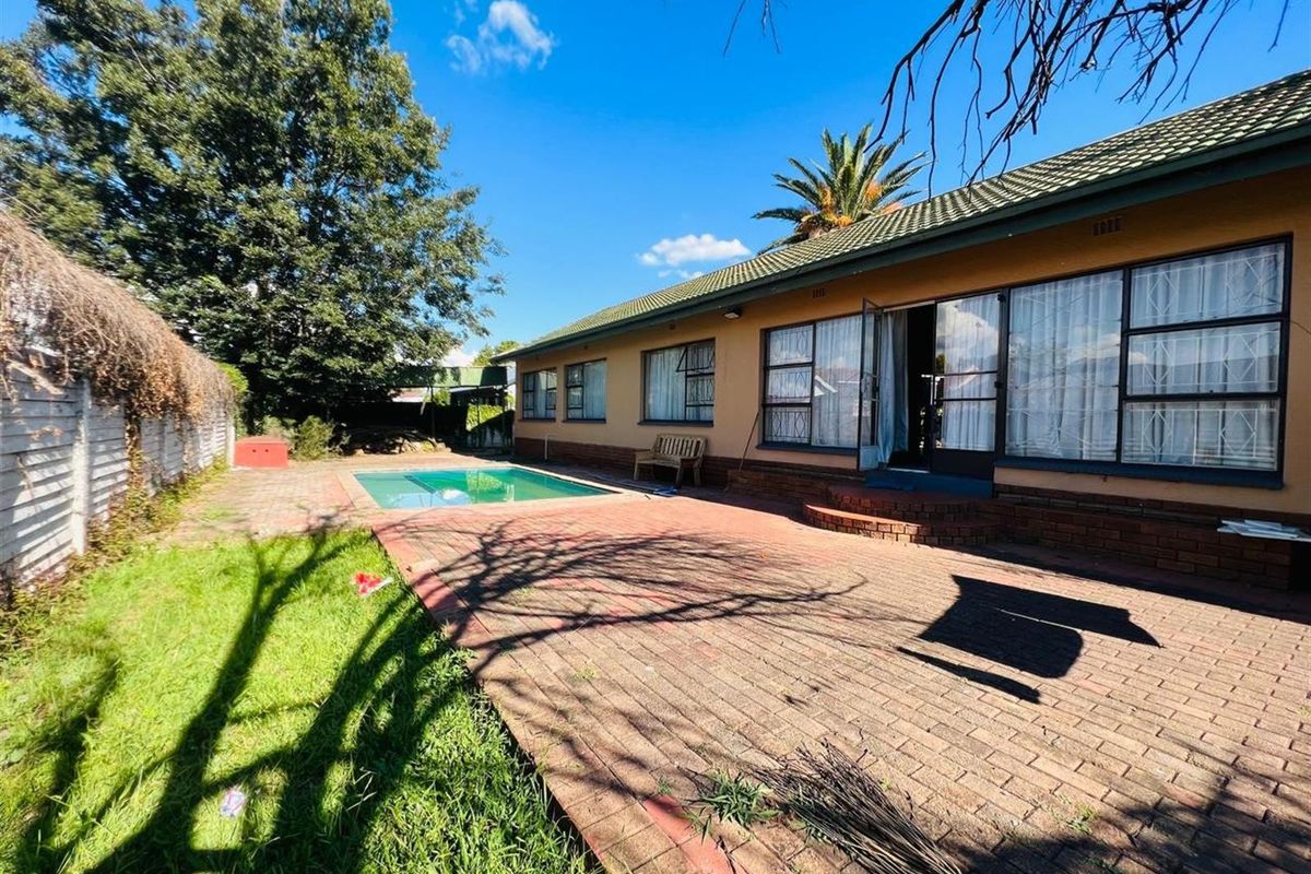 Rear exterior view featuring a swimming pool, brick paved patio area, and established garden with a tiled roof house facade.