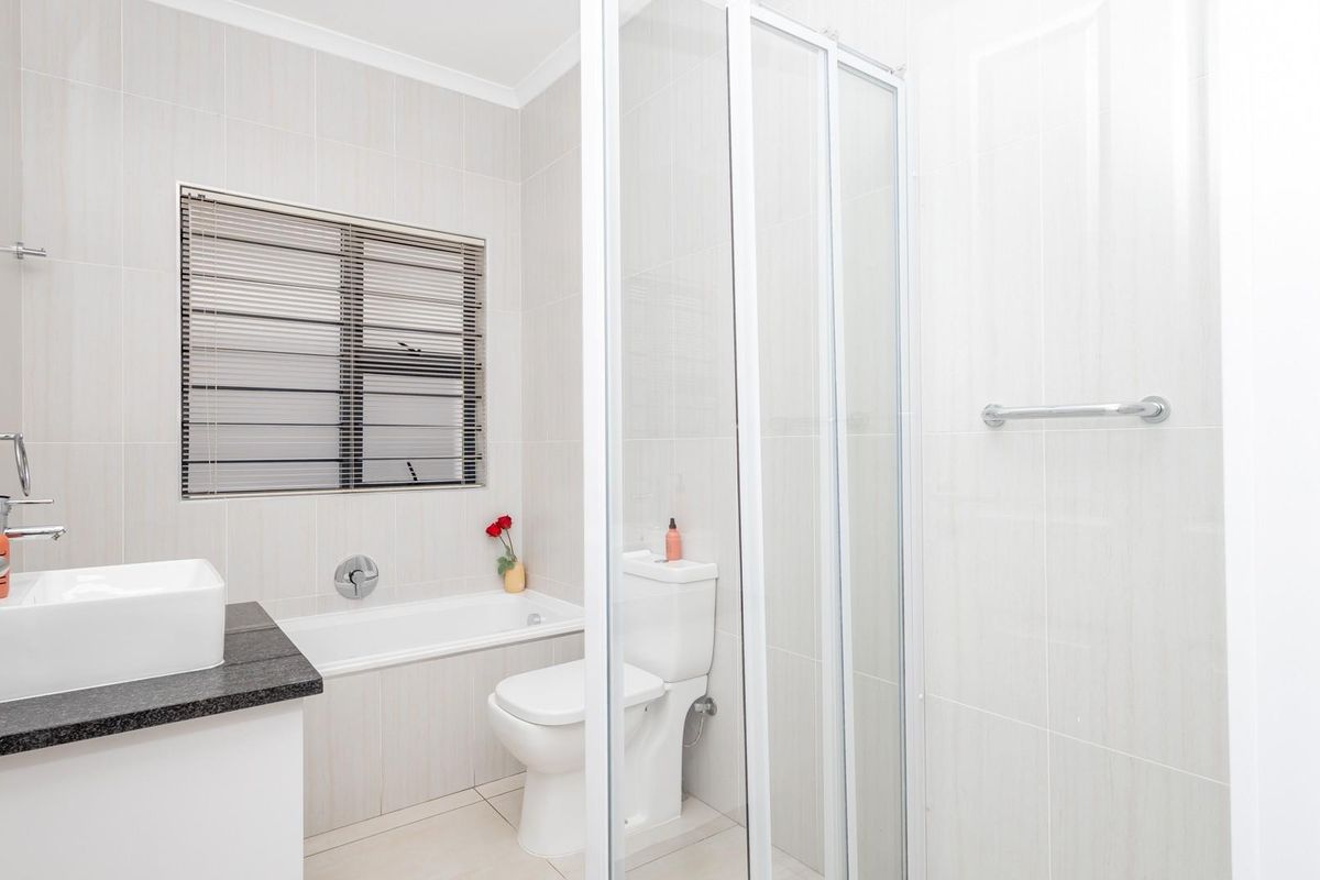 A modern, well-maintained bathroom featuring a built-in bathtub, separate shower enclosure, vanity basin with granite countertop, and neutral floor-to-ceiling wall tiles.
