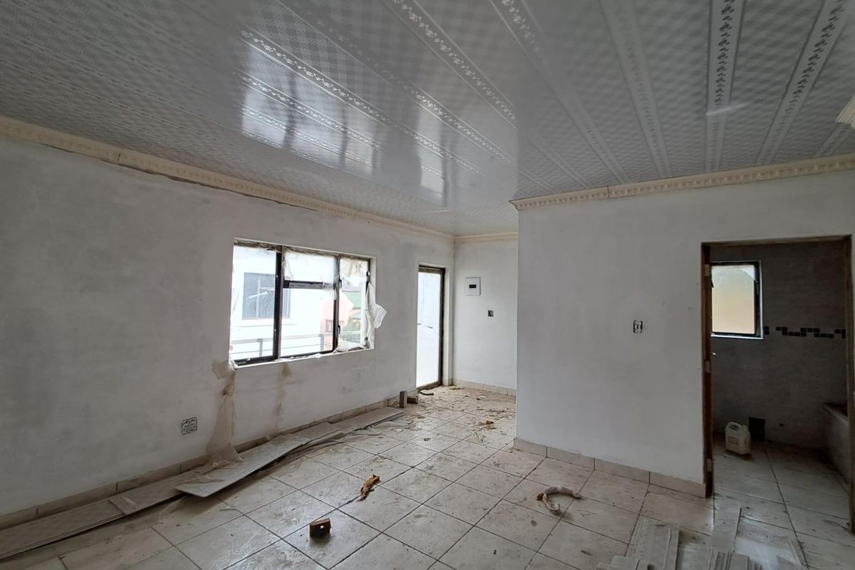 An unfinished interior space featuring tiled flooring, a decorative ceiling, and window openings, currently undergoing renovation or construction work.