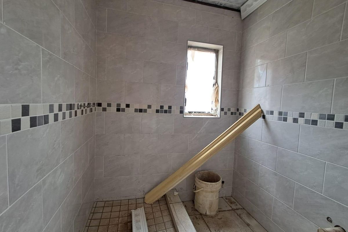 A small, unfinished bathroom space featuring grey wall tiling with a decorative mosaic border and tiled flooring, currently undergoing renovation.