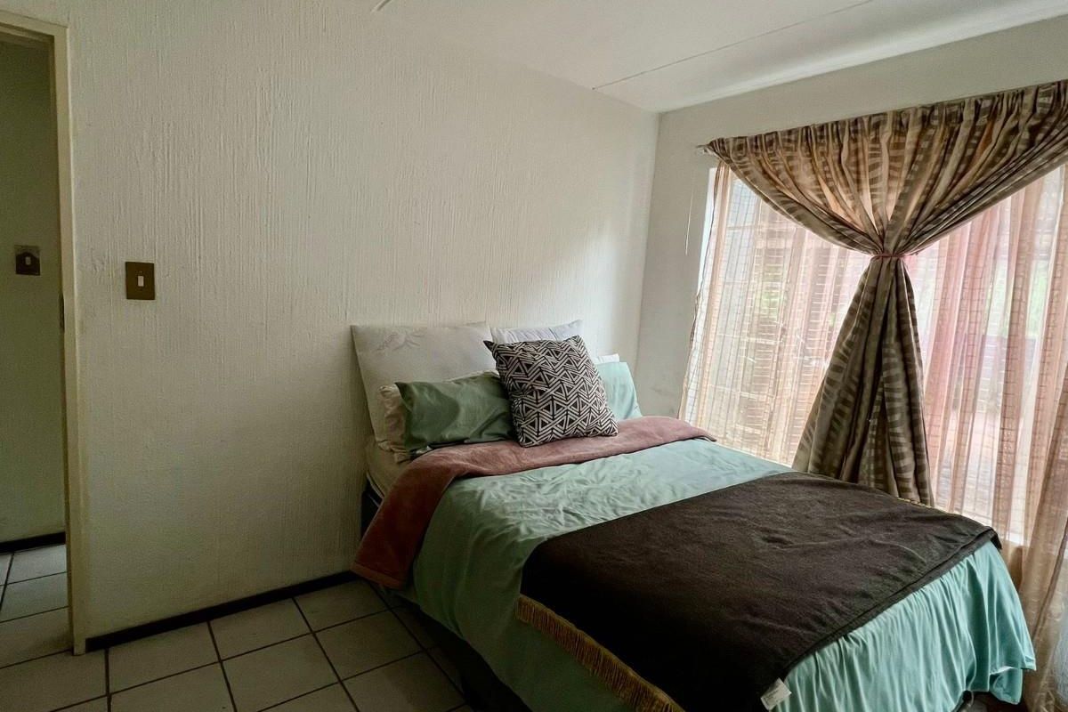 A functional bedroom featuring tiled flooring, textured walls, and a large window with curtain treatments.