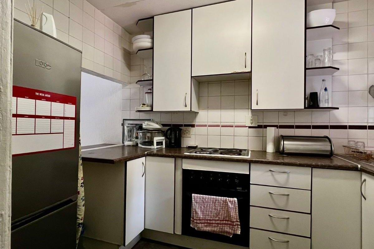 A compact kitchen featuring dated white cabinetry, laminate countertops, a built-in oven with hob, and tiled wall finishes.