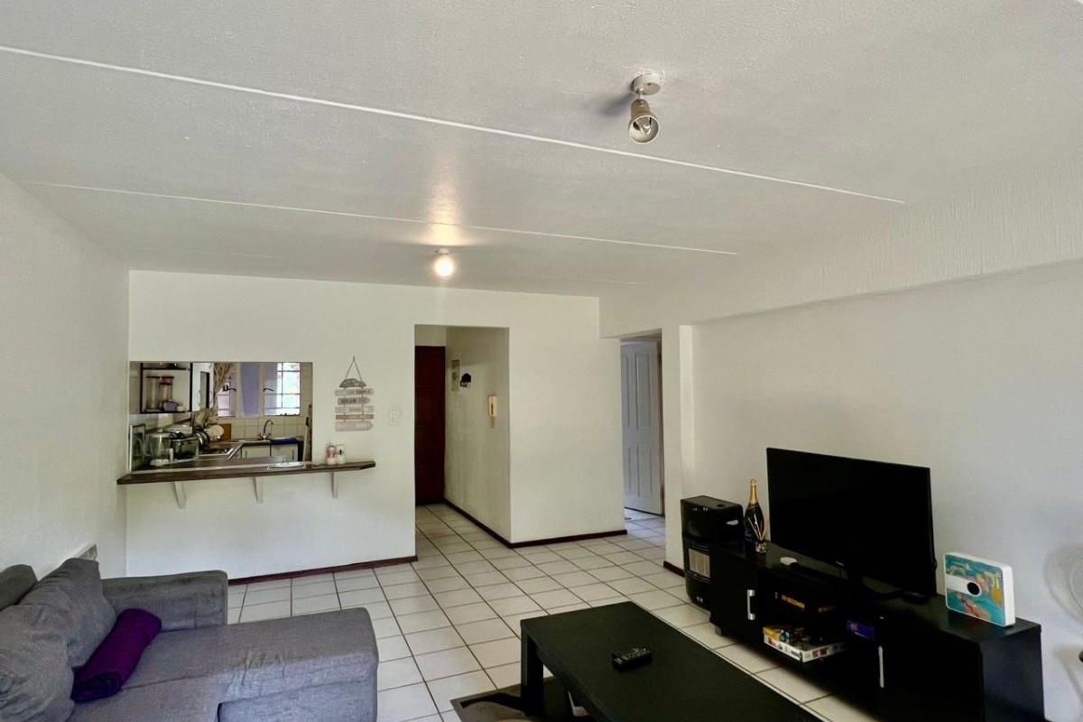 Open plan living area featuring tiled flooring and a convenient kitchen pass-through window with a breakfast bar, creating a functional and connected living space.