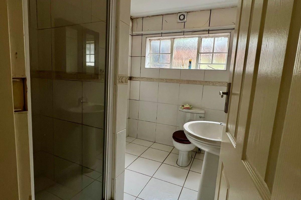 A dated bathroom featuring a pedestal basin, toilet, and a separate shower enclosure with tiled finishes throughout.