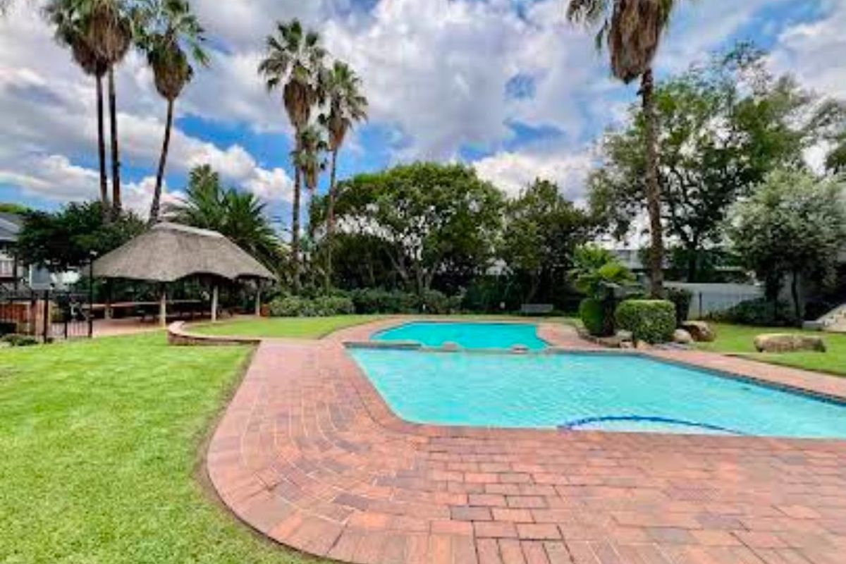 A well-maintained communal pool area featuring brick paving, a thatched lapa for outdoor entertaining, and established garden landscaping.