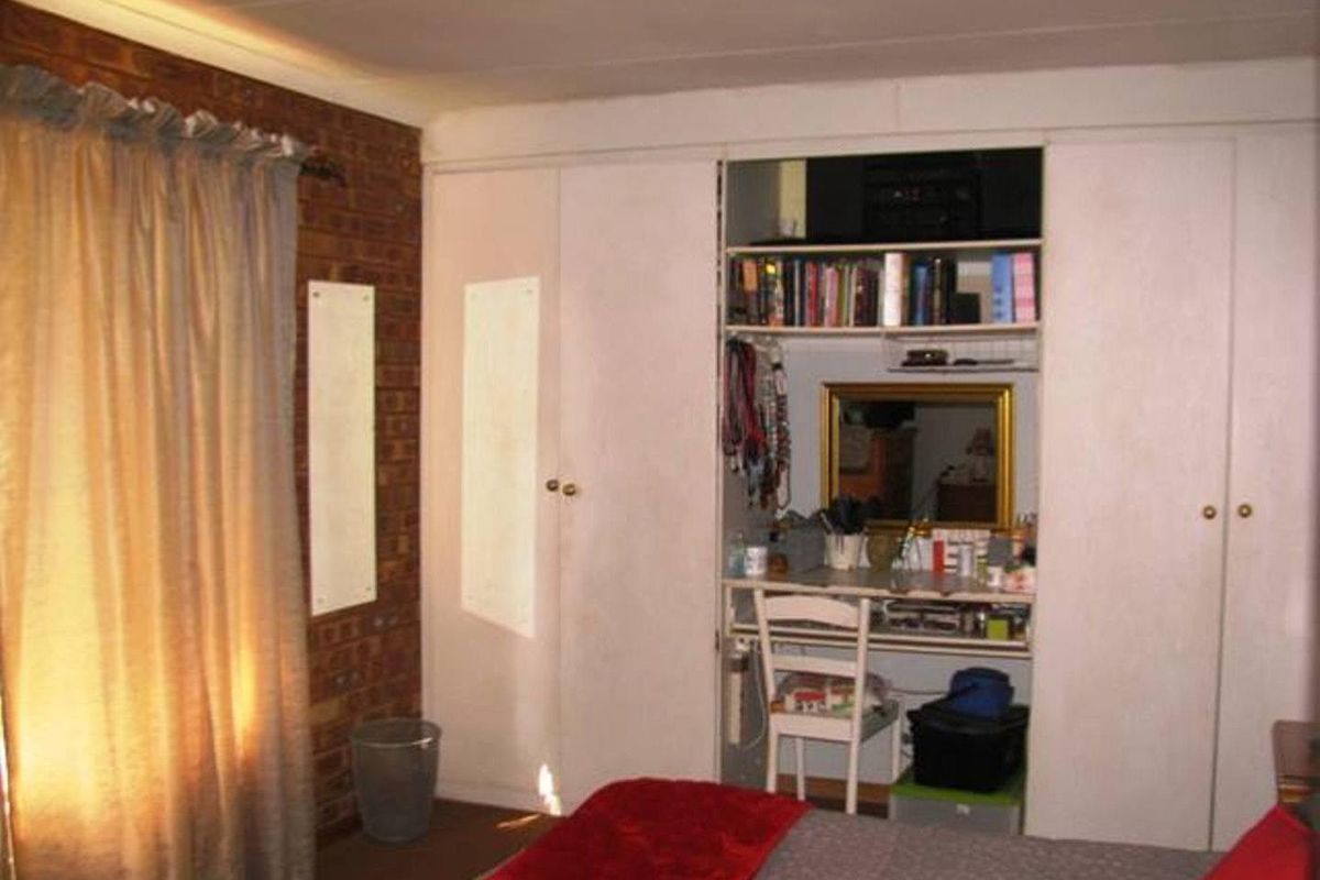 A bedroom featuring built-in cupboards with an integrated vanity area and exposed brick wall detailing.
