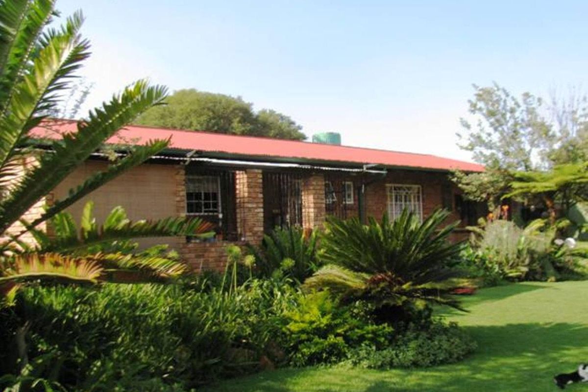 A view of the farm house exterior featuring a red metal roof, brick facade, and established garden surroundings.