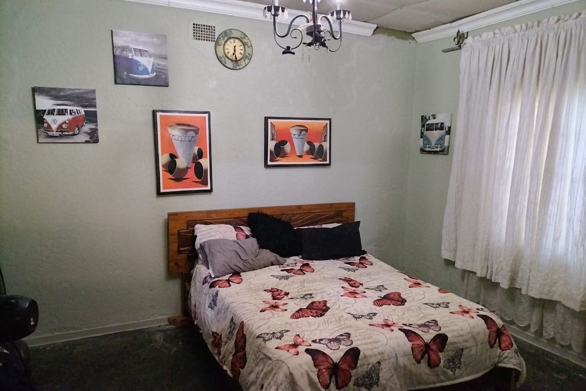 A bedroom featuring a built-in wooden headboard, crown molding, and a central chandelier, with a window dressed in curtains.