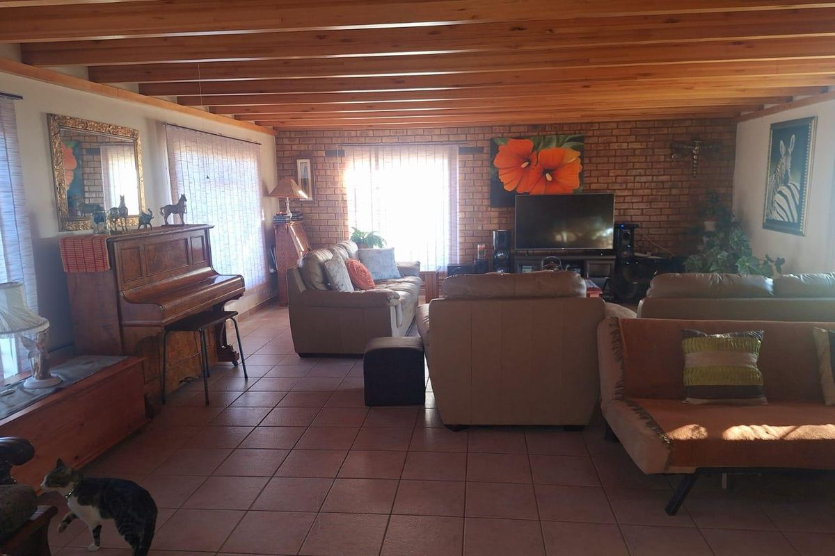 Spacious living room featuring exposed timber beam ceilings, face-brick feature wall, and tiled flooring, creating a warm and rustic atmosphere.
