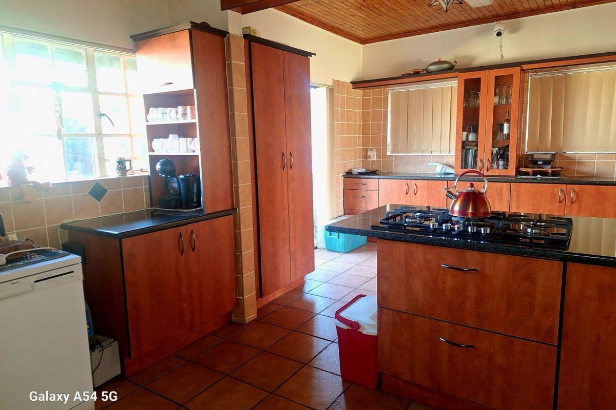 A functional kitchen featuring wooden cabinetry, granite countertops, a built-in gas hob, and tiled flooring with a timber-paneled ceiling.
