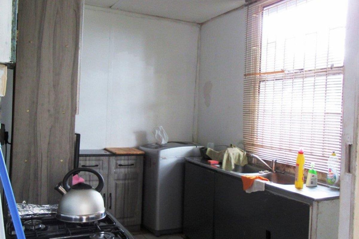 A compact kitchen area featuring basic cabinetry, a stainless steel sink, and a gas stove, with tiled flooring and natural light from a window.