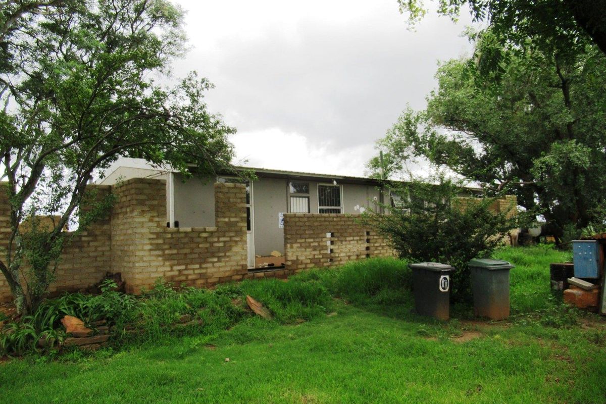 Exterior view of a farm building featuring unfinished brick walls and surrounding garden area, requiring maintenance and completion of exterior finishes.