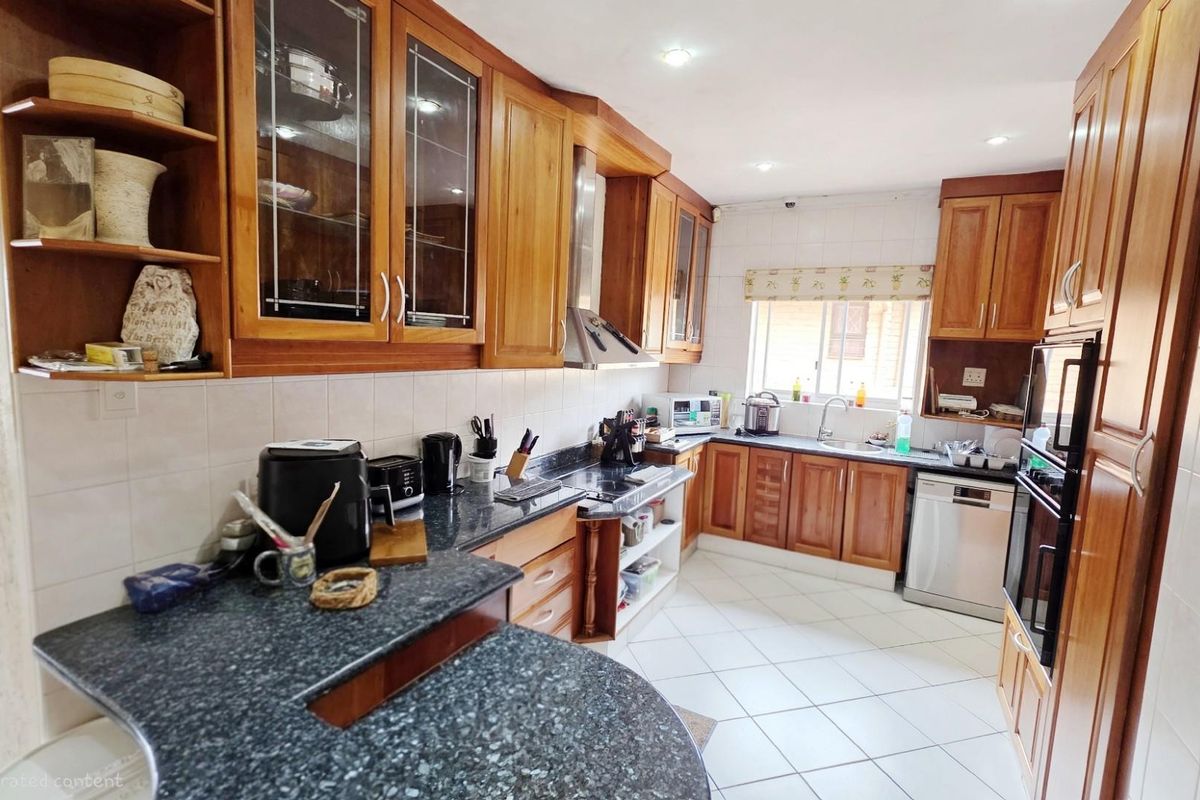 A functional kitchen featuring wooden cabinetry, granite countertops, tiled flooring, and built-in appliances including an oven and extractor fan.
