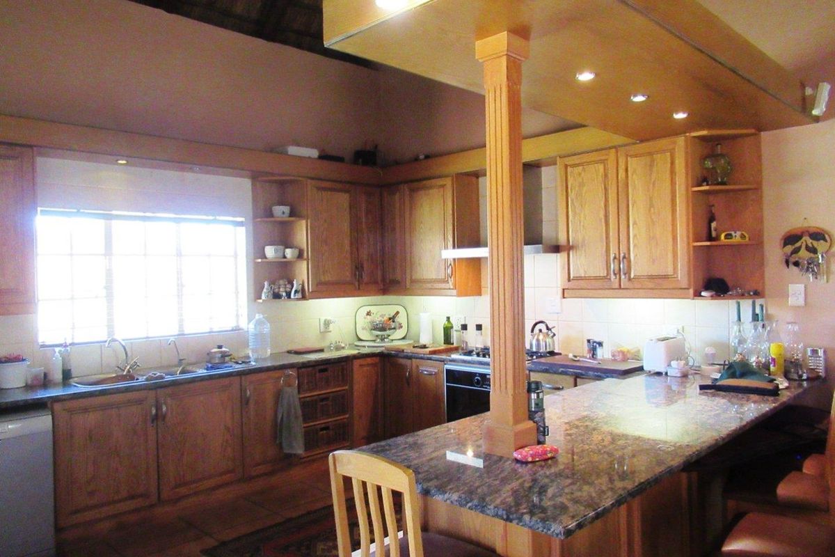 Spacious farm-style kitchen featuring solid wood cabinetry, granite countertops, a central breakfast island, and a high vaulted thatched ceiling.