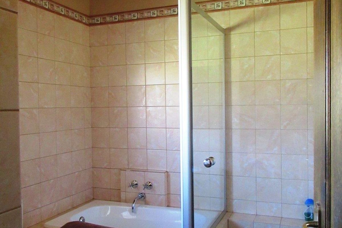 A functional bathroom featuring a built-in bathtub and a separate glass-enclosed shower with neutral wall tiling.