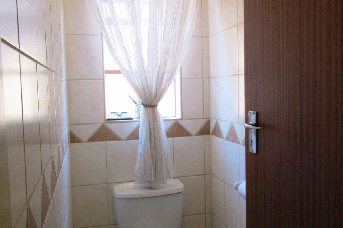 A compact guest toilet featuring ceramic wall and floor tiles with a neutral decorative border.