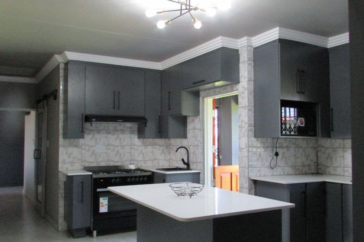 Modern kitchen featuring dark grey cabinetry, a central island with a white countertop, tiled backsplash, and a built-in gas stove with extractor fan.