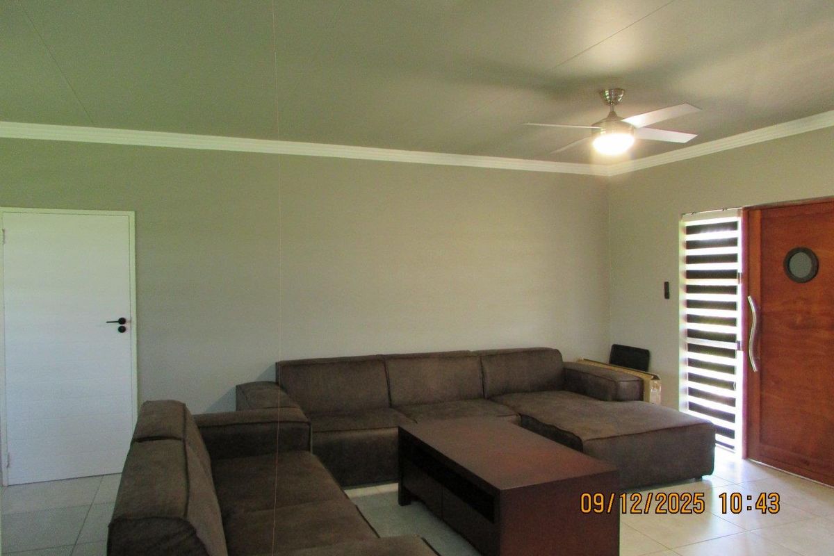 A living room featuring tiled flooring, crown molding, a ceiling fan with integrated lighting, and a wooden door with a circular window.