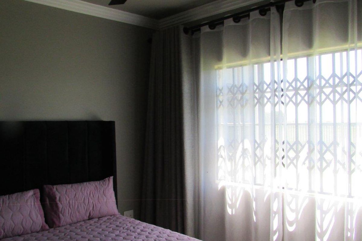 A well-maintained bedroom featuring a modern ceiling fan, crown molding, and a window fitted with a security gate.