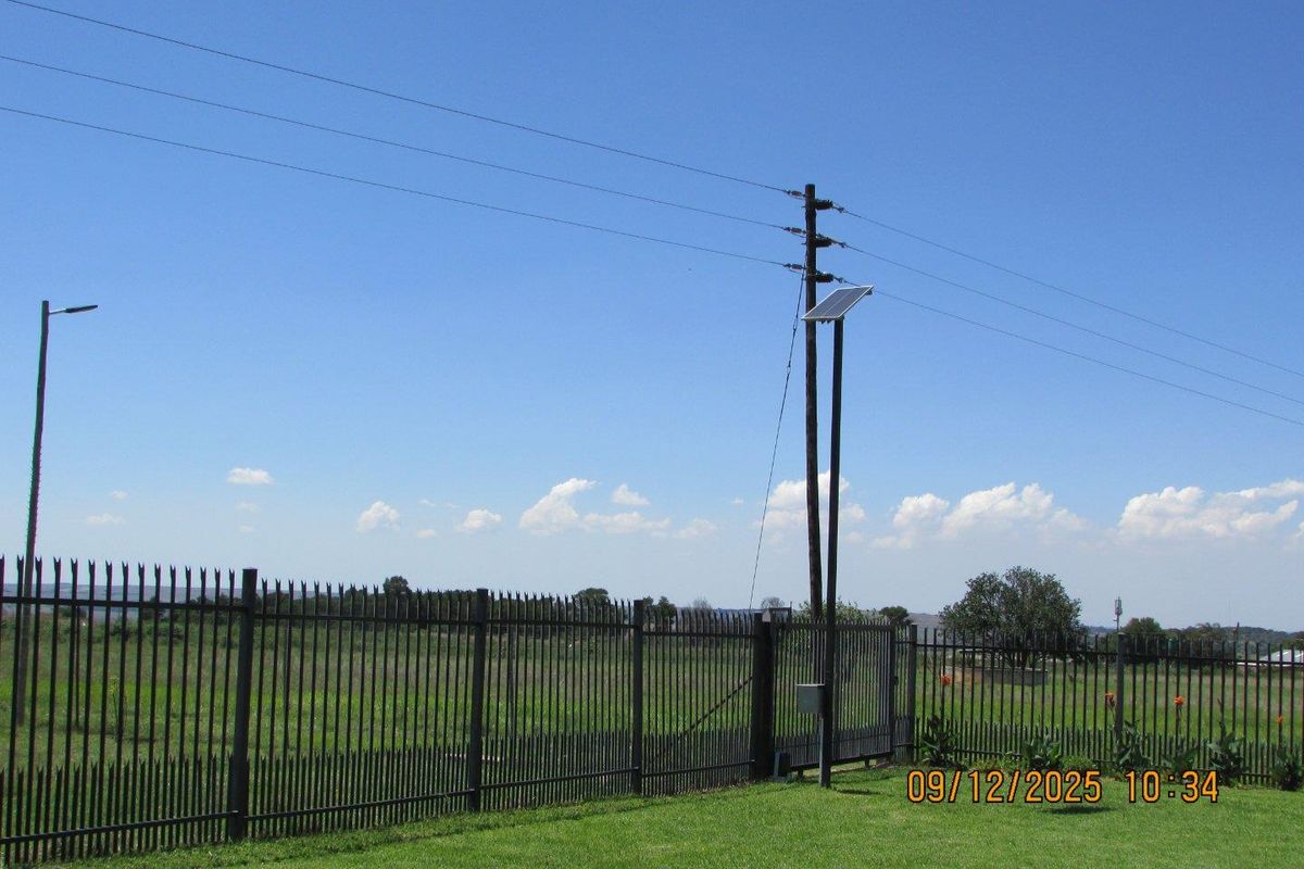 A view of the property perimeter featuring a secure metal fence, utility pole with solar panel, and outdoor lighting.