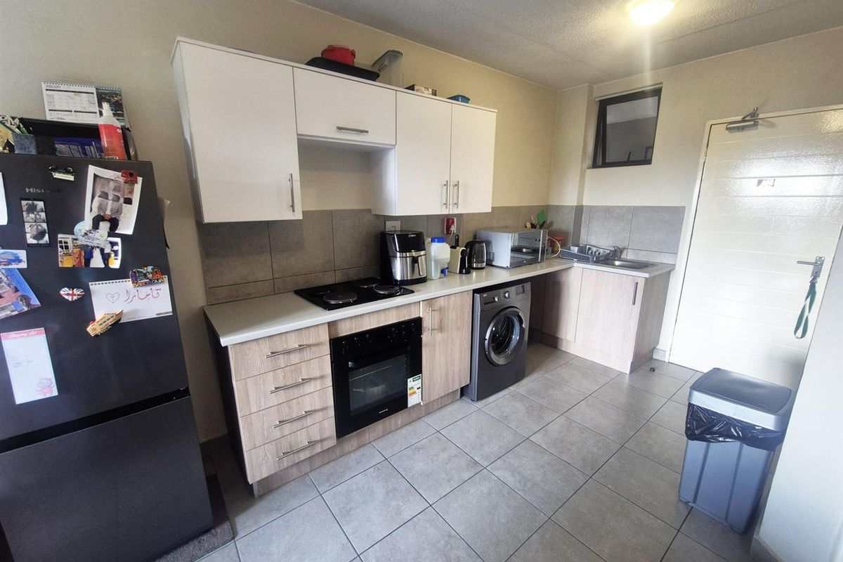 A functional kitchen featuring light wood-look cabinetry, tiled flooring, a built-in oven and hob, and integrated space for a washing machine.