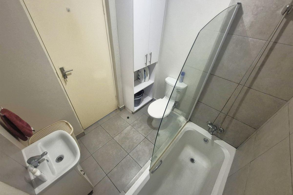 A functional bathroom featuring a bathtub with a glass shower screen, a pedestal basin, a toilet, and built-in storage cabinetry.