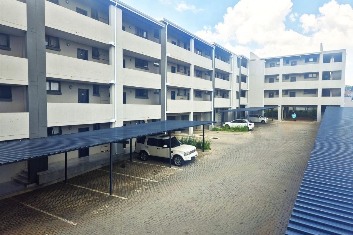 Exterior view of a multi-story apartment complex featuring paved parking areas with covered carports and concrete building facades.