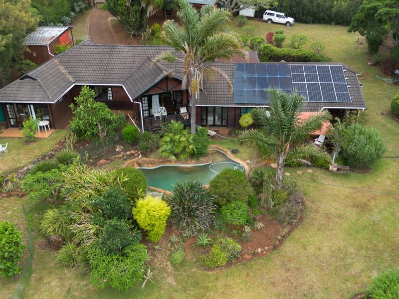 Aerial view of a farm property featuring a house with a tiled roof, solar panels, a swimming pool, and established garden landscaping.