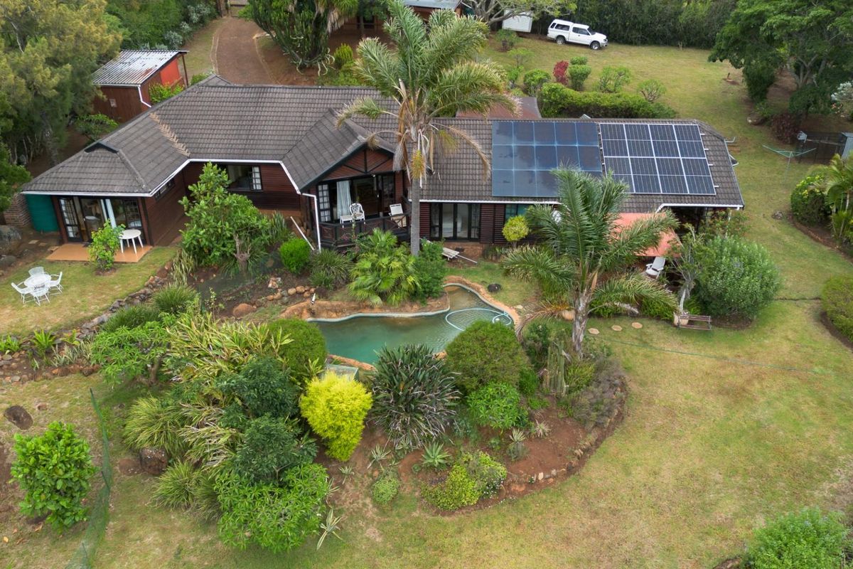 Aerial view of a farm property featuring a house with a tiled roof, solar panels, a swimming pool, and established garden landscaping.