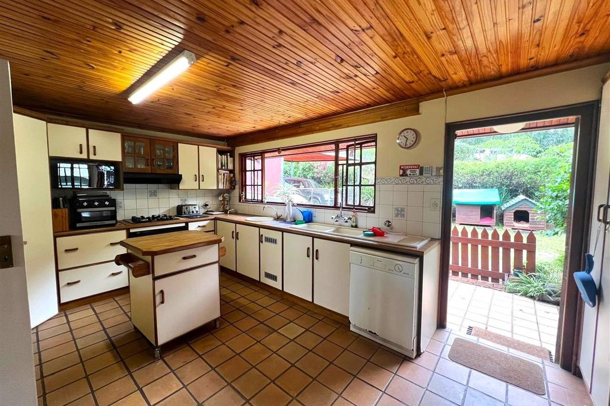 A functional kitchen featuring wooden ceiling paneling, tiled flooring, built-in cabinetry, and direct access to the rear garden area.