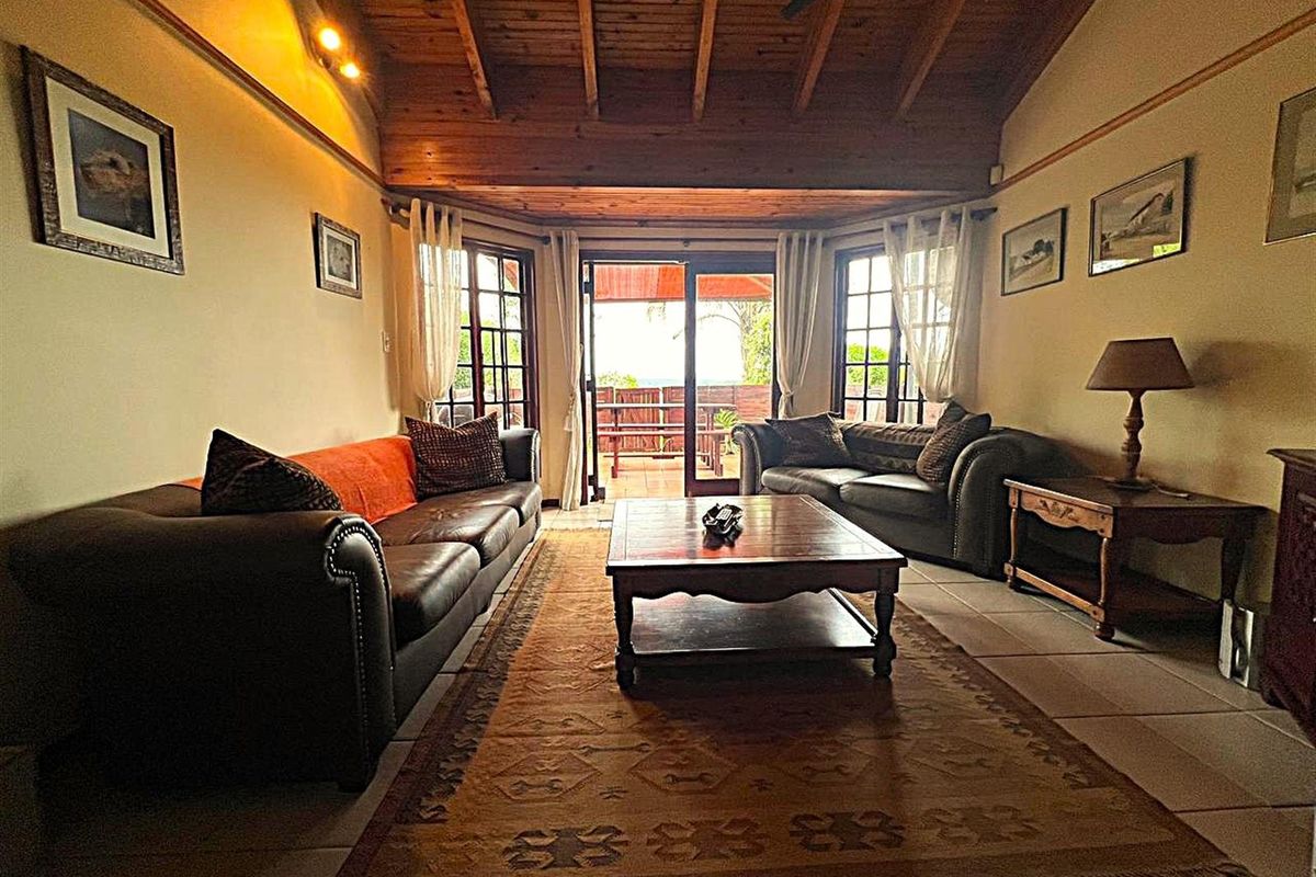 A cozy living room featuring a high exposed timber beam ceiling, tiled flooring, and sliding glass doors that open onto an outdoor patio area.