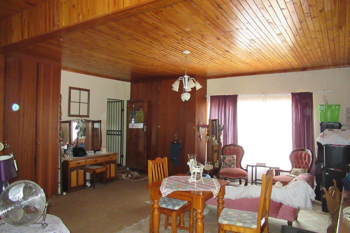 A living area featuring extensive wood paneling on the ceiling and walls, with large windows providing natural light and carpeted flooring throughout.