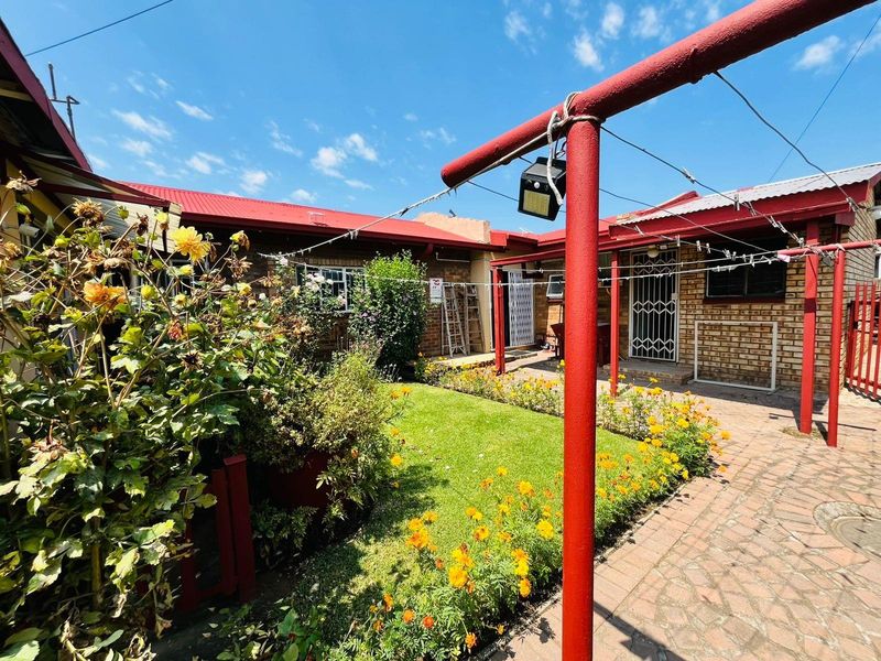 A rear courtyard area featuring a small lawn, flower beds, paved pathways, and red metal structural supports for a clothesline.