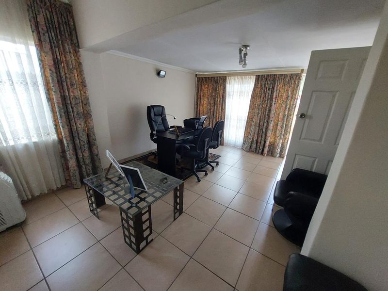A functional home office space featuring tiled flooring, large windows with floor-to-ceiling curtains, and a standard interior door.
